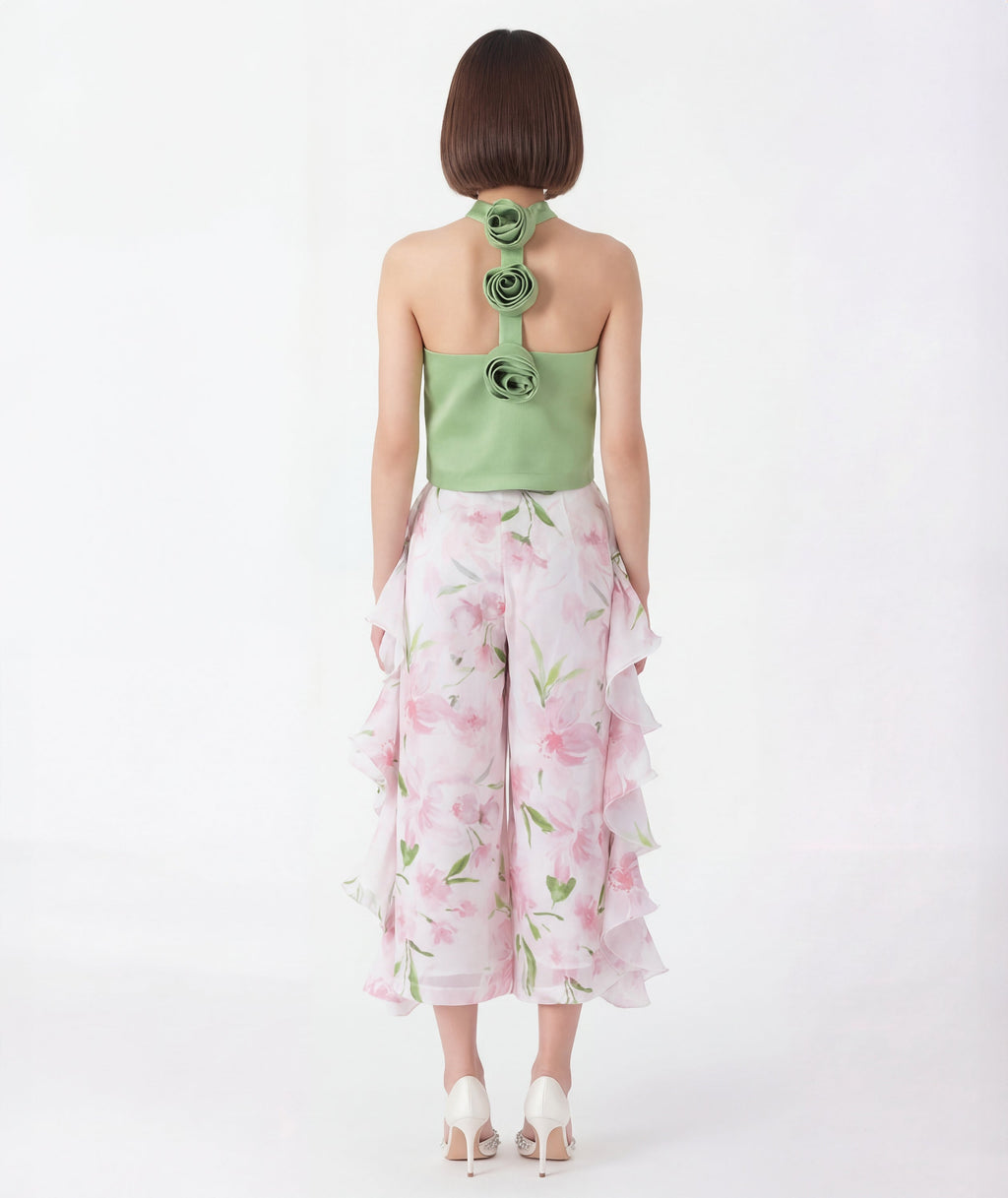 Woman wearing a green flower detail top with floral patterns and white pants on a white background