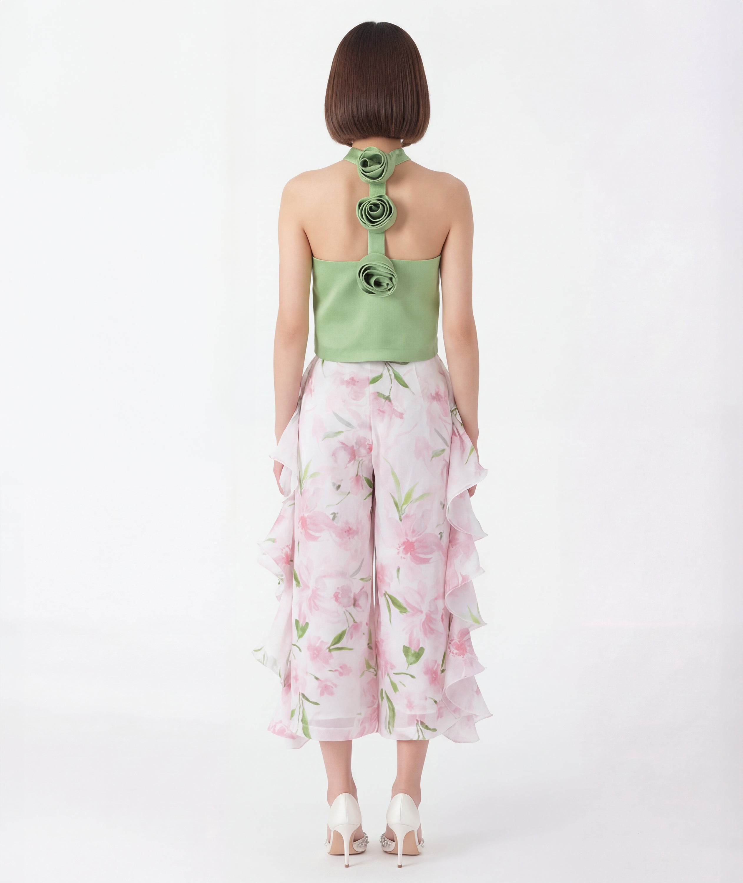 Woman wearing a green flower detail top with floral patterns and white pants on a white background