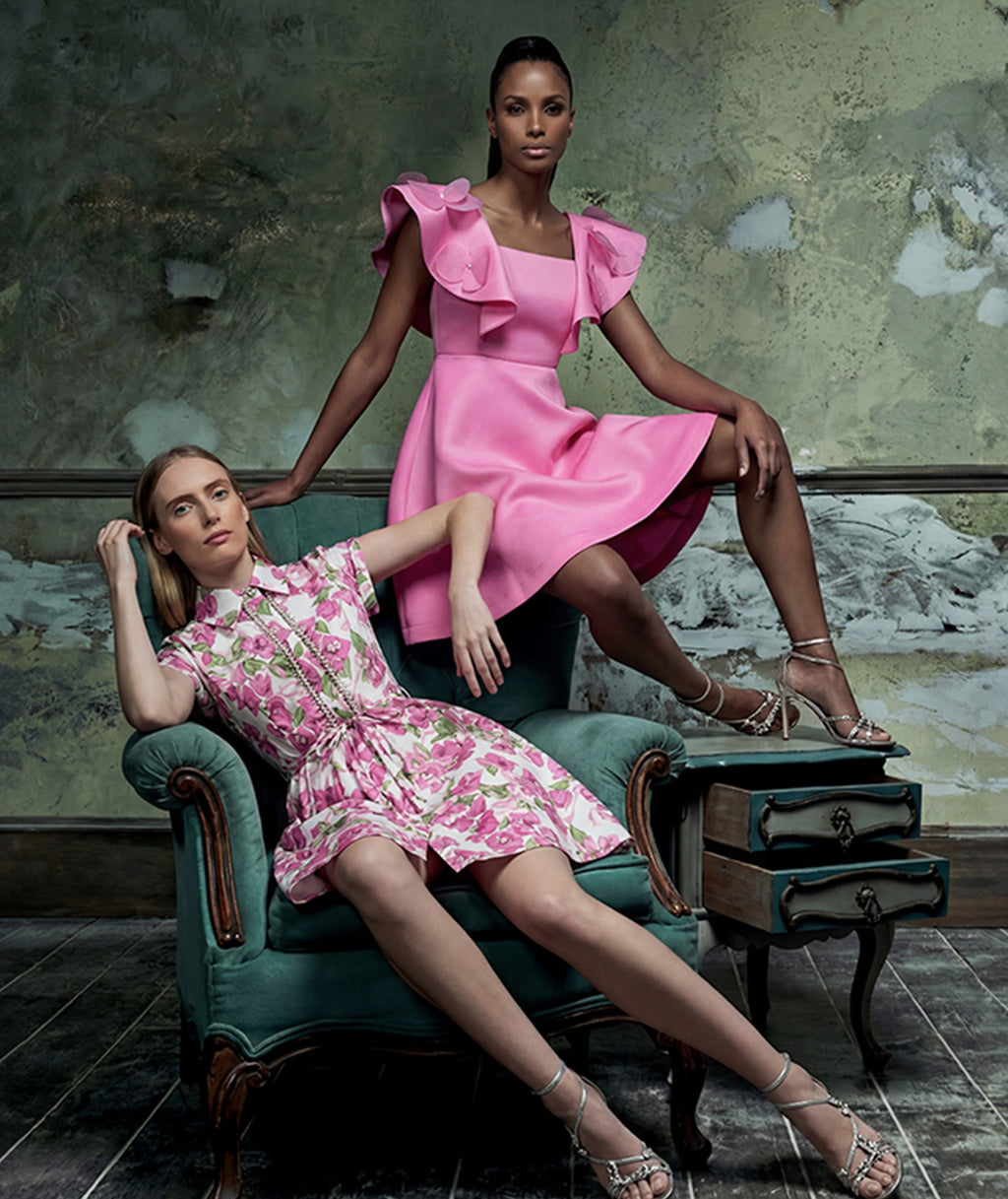 Two women in pink dresses posing in an indoor setting with a textured wall.