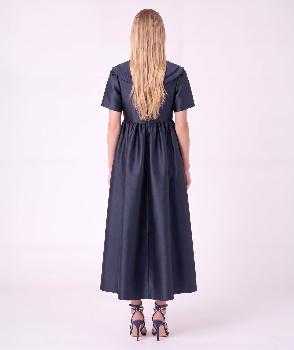 Back view of the Enchanting Brooch Women’s Dress from Mama Luma’s Suva Maia Collection, featuring a layered collar and full navy satin skirt.