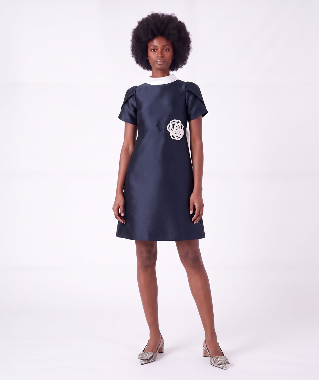 Front view of the Suva Maia Flower Women’s Dress in navy featuring an ivory high collar and sculptural flower appliqué by Mama Luma.
